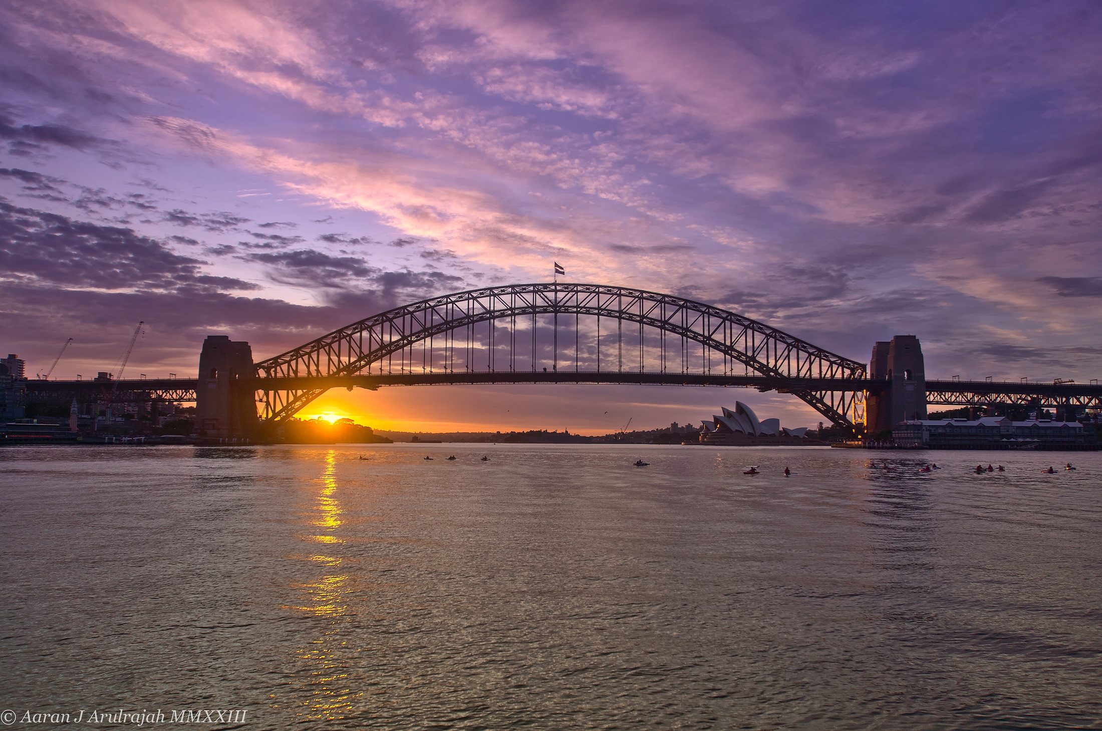 Sunrise breaking purple and gold over Sydney Harbour, the Opera House and Harbour Bridge in silhouette